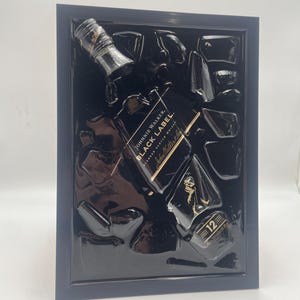 May include: Black framed artwork featuring a Johnnie Walker Black Label Scotch Whisky bottle and ice cubes. The bottle is black with gold lettering and a gold label that reads "12". The artwork is set against a black background.