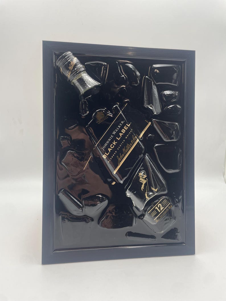 May include: Black framed artwork featuring a Johnnie Walker Black Label Scotch Whisky bottle and ice cubes. The bottle is black with gold lettering and a gold label that reads "12". The artwork is set against a black background.