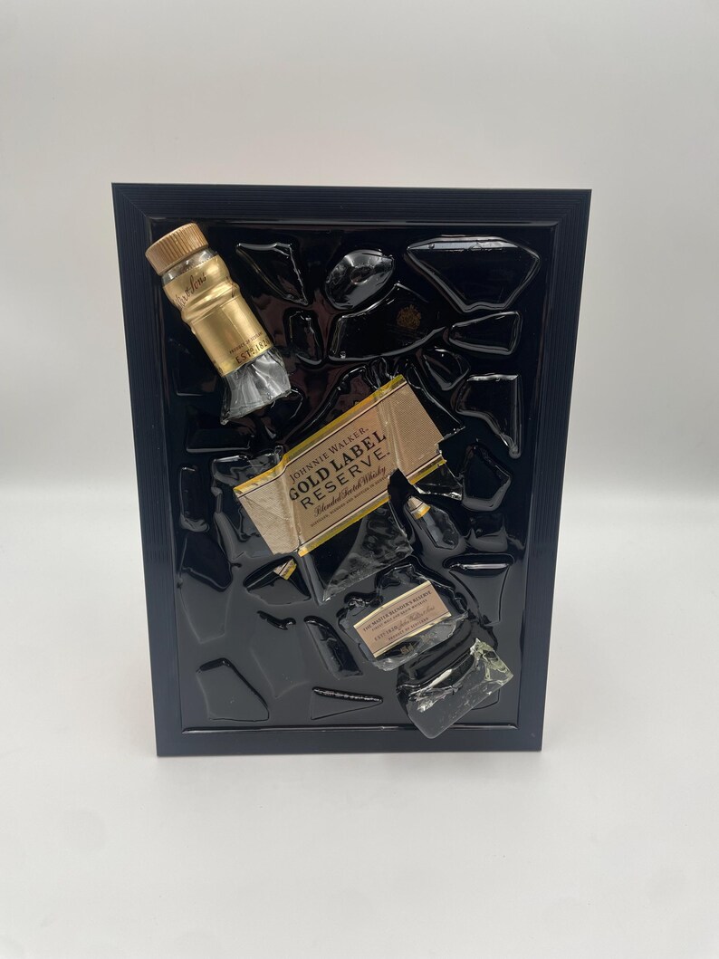 Pu&ograve; includere: Un'opera d'arte incorniciata con una bottiglia e un'etichetta di whisky Johnnie Walker Gold Label Reserve, su sfondo nero. Il tappo dorato e l'etichetta della bottiglia sono visibili, all'interno di una cornice nera.