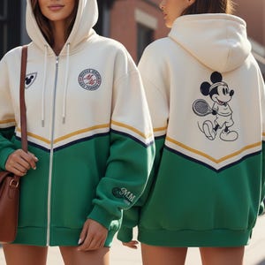 Puede incluir: Sudadera con capucha crema con cremallera y detalles en verde y amarillo. Cuenta con un parche de Mickey Mouse en el pecho y un gráfico más grande de Mickey jugando al tenis en la espalda. Las mangas tienen las iniciales "MM".