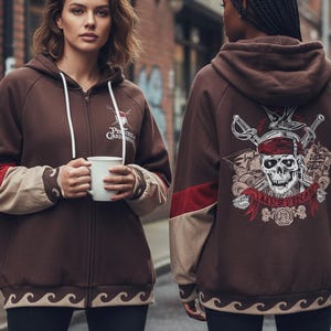 May include: Brown zip-up hoodie with a pirate-themed design. The hoodie features a skull and crossbones graphic on the back, with red and tan accents on the sleeves. The front has the text "Pirates of the Caribbean".