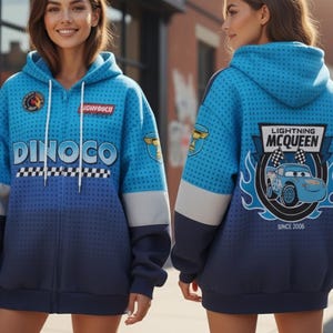 May include: Blue zip-up hoodie with Dinoco and Lightning McQueen designs. The front features the Dinoco logo and text, the back displays Lightning McQueen with flames and the text "Lightning McQueen Since 2006". The hoodie has a gradient design, with a blue and grey colour scheme.