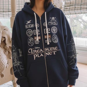 May include: Navy blue zip-up hoodie with white drawstring and multiple white graphic patches. The hoodie features the text "Disney TREASURE PLANET" in white, with a spaceship design on the sleeves.