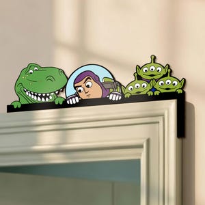 Puede incluir: Una decoración negra para el marco de la puerta con personajes de la película animada Toy Story. Los personajes incluyen a Rex el dinosaurio, Buzz Lightyear y tres pequeños hombres verdes. Los personajes son de color verde, morado, azul y blanco.