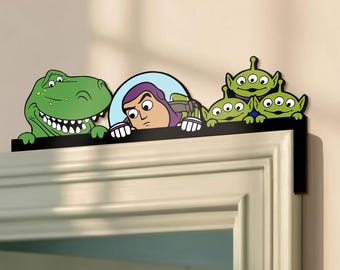May include: A black door frame decoration featuring characters from the animated film Toy Story. The characters include Rex the dinosaur, Buzz Lightyear, and three Little Green Men. The characters are in green, purple, blue, and white.