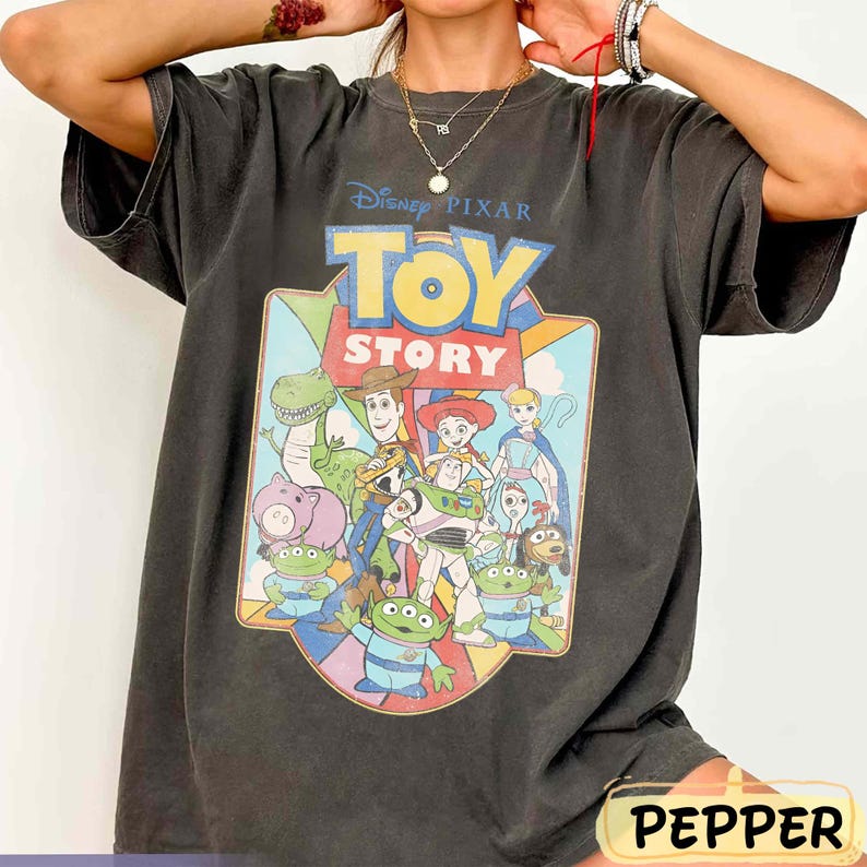 Puede incluir: Camiseta gris oscuro con el logotipo y los personajes de "Toy Story" de Disney Pixar. El gr&aacute;fico incluye a Woody, Buzz Lightyear y otros personajes de la pel&iacute;cula animada. La camiseta tiene un aspecto vintage y desgastado.
