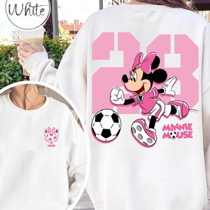 May include: White sweatshirt with a pink graphic of Minnie Mouse playing football, with the number 23 in pink. A football is also visible. The sweatshirt has the text "Minnie Mouse" in pink.