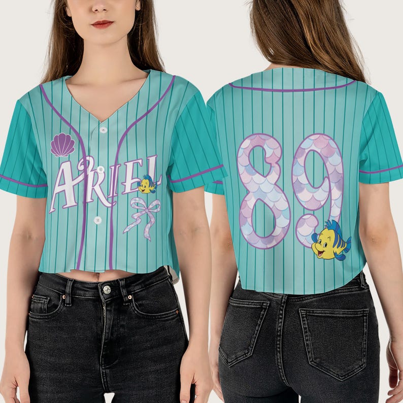 May include: A teal and purple baseball jersey with the word "Ariel" and a seashell on the front. The back of the jersey has the number "89" with a mermaid tail design and a cartoon Flounder.