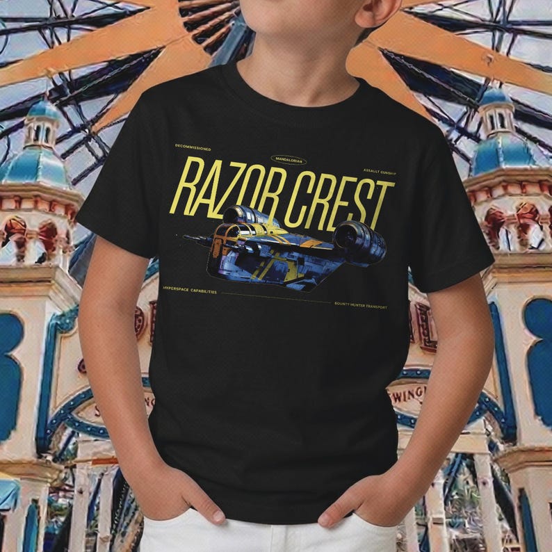 May include: Black t-shirt featuring the text "RAZOR CREST" in yellow, with a blue and yellow spaceship graphic. The shirt also includes text that reads "HYPERSPACE CAPABILITIES" and "BOUNTY HUNTER TRANSPORT".