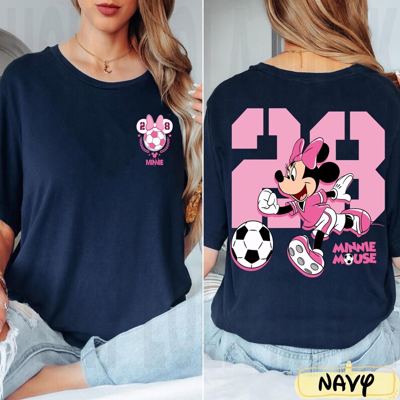 May include: Navy blue t-shirt with a pink Minnie Mouse soccer design. The front has a soccer ball with the number 28 and "Minnie". The back shows Minnie Mouse in a soccer uniform with the number 28 and a soccer ball.