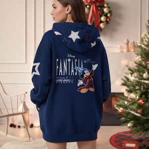 May include: A navy blue hooded sweatshirt featuring the Disney Fantasia Sorcerer's Apprentice Mickey Mouse design. The back of the sweatshirt has white star graphics and the Disney Fantasia logo. The sweatshirt has a kangaroo pocket.