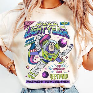 Puede incluir: Camiseta color crema con un gráfico de Buzz Lightyear con traje espacial. El diseño incluye las palabras "Buzz Lightyear", "Space Ranger" y "To Infinity and Beyond". La camiseta tiene cuello redondo y mangas cortas.