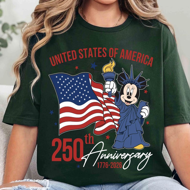 May include: Dark green t-shirt featuring a graphic of Mickey Mouse dressed as the Statue of Liberty, holding a torch and an American flag. The text reads "United States of America" and "250th Anniversary 1776-2026".