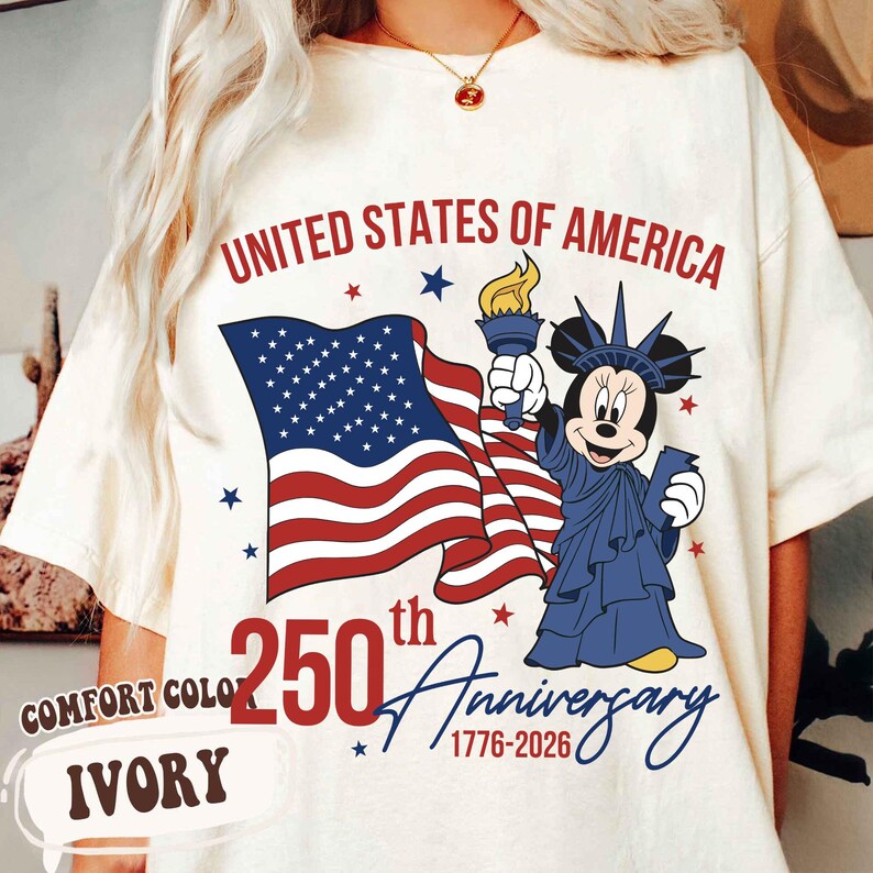 May include: Ivory-colored t-shirt featuring a graphic of the American flag, Minnie Mouse as the Statue of Liberty, and text that reads "United States of America 250th Anniversary 1776-2026." The shirt is labeled "Comfort Color."