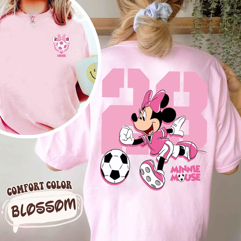 May include: Pale pink Comfort Colors t-shirt featuring a Minnie Mouse soccer design. The back displays a large pink number 23 and a Minnie Mouse illustration. The front has a small soccer graphic with the text "MINNIE".