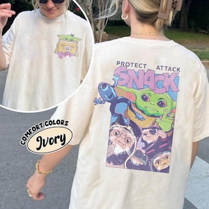 May include: Ivory-colored t-shirt with a graphic of a green alien character and the text "PROTECT ATTACK SNACK". The shirt also features a smaller graphic on the front pocket. The shirt is made of Comfort Colors material.