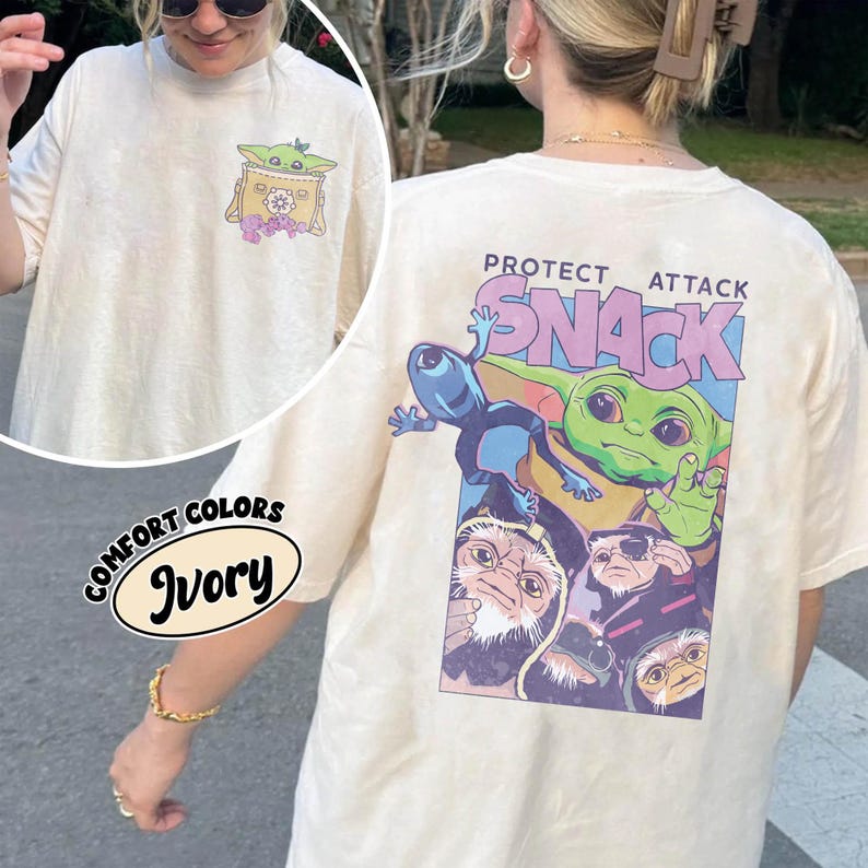 May include: Ivory-colored t-shirt with a graphic of a green alien character and the text "PROTECT ATTACK SNACK". The shirt also features a smaller graphic on the front pocket. The shirt is made of Comfort Colors material.