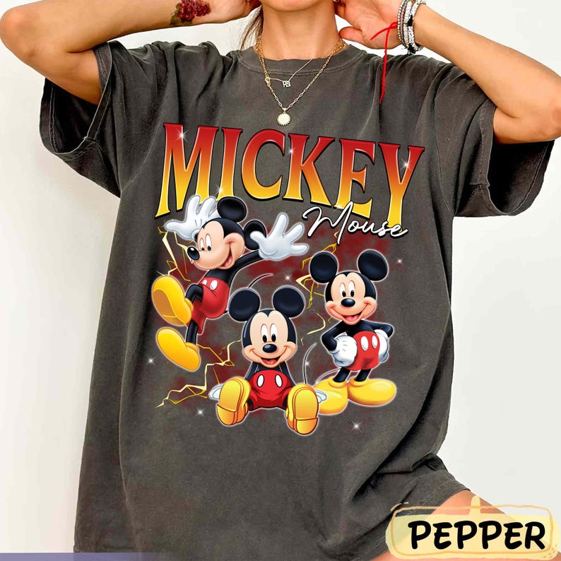 May include: Dark grey t-shirt with a graphic of Mickey Mouse in three poses. The text "Mickey Mouse" is in red and yellow. The shirt has a vintage, distressed appearance.