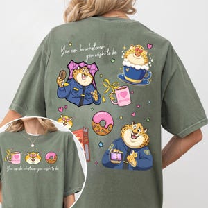 May include: Olive green t-shirt featuring cartoon leopard illustrations. The design includes a leopard character in a police uniform, donuts, coffee, and the text "You can be whatever you wish to be."