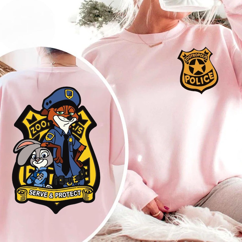 May include: Pale pink sweatshirt with a Zootropolis Police badge on the front and a larger graphic on the back. The graphic features Nick Wilde, Judy Hopps, and the words "Serve & Protect".