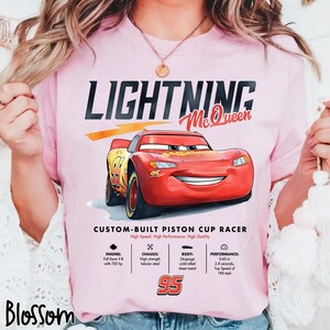 Puede incluir: Camiseta rosa con un dise&ntilde;o de Rayo McQueen, un coche de carreras rojo con el n&uacute;mero 95. La camiseta incluye el texto "LIGHTNING McQueen" y "CUSTOM-BUILT PISTON CUP RACER".