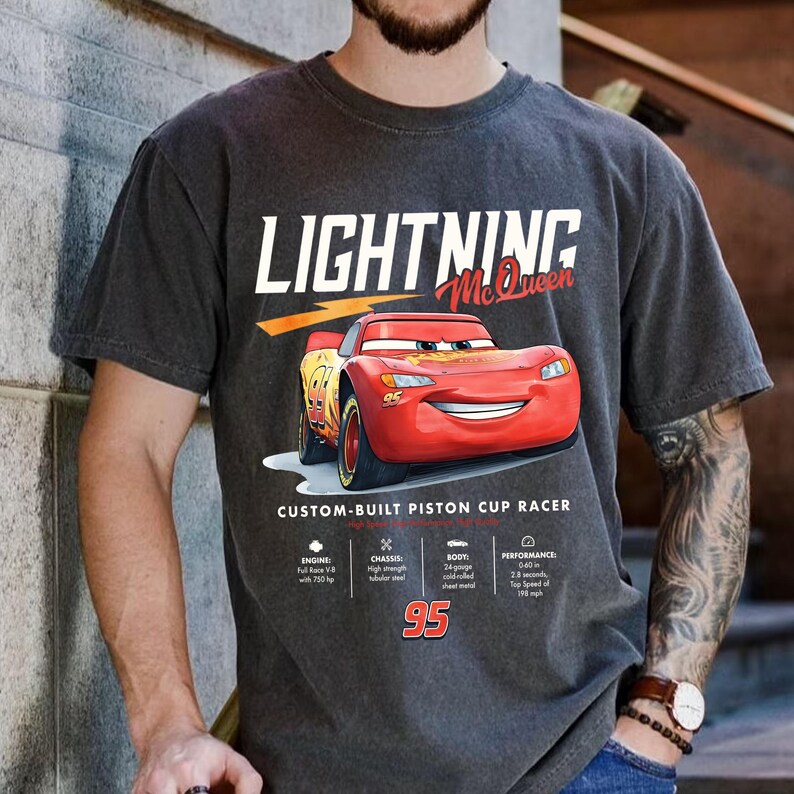 Puede incluir: Camiseta gris oscuro con Lightning McQueen de la pel&iacute;cula Cars. El dise&ntilde;o incluye el texto "LIGHTNING McQueen" y "CUSTOM-BUILT PISTON CUP RACER", adem&aacute;s de especificaciones del coche.