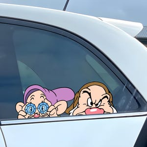 May include: Car window sticker featuring two cartoon characters. One character wears a purple hat and holds blue gem-like objects. The other character has a grumpy expression. The stickers are white-bordered and designed for car window application.