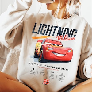 Puede incluir: Sudadera color crema con un gr&aacute;fico de Rayo McQueen, un coche de carreras rojo con el n&uacute;mero 95. El texto "LIGHTNING McQueen" est&aacute; encima del coche. Las especificaciones t&eacute;cnicas est&aacute;n debajo.