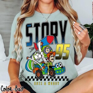 May include: A light green t-shirt featuring a graphic from the movie Toy Story. The graphic includes the words "Toy Story 95", Buzz Lightyear, and Woody riding a vehicle. The words "Buzz & Woody" are also included.