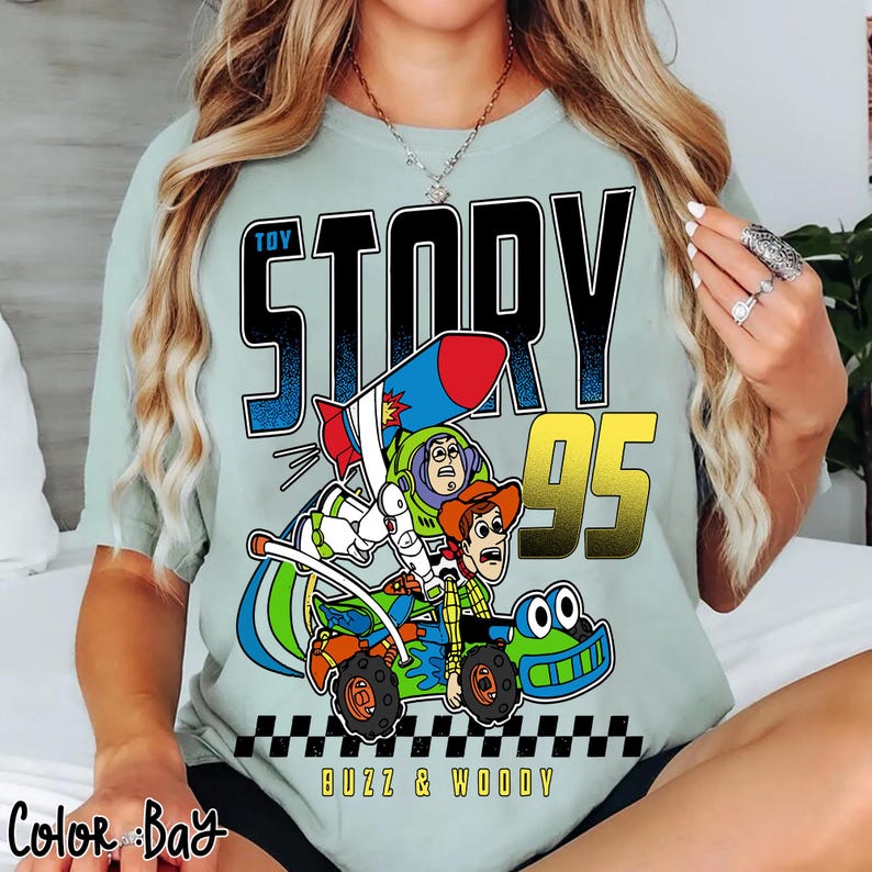 May include: A light green t-shirt featuring a graphic from the movie Toy Story. The graphic includes the words "Toy Story 95", Buzz Lightyear, and Woody riding a vehicle. The words "Buzz & Woody" are also included.