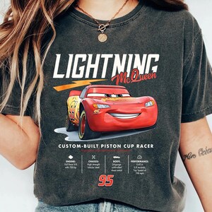 Puede incluir: Camiseta gris oscuro con Lightning McQueen de la pel&iacute;cula Cars. El dise&ntilde;o incluye el texto "LIGHTNING McQueen" y detalles t&eacute;cnicos del coche. El n&uacute;mero 95 se muestra de forma destacada. Una prenda de vestir informal.