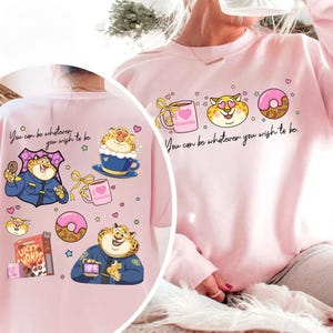 May include: Pink sweatshirt with a cartoon leopard design and the text "You can be whatever you wish to be." The design includes a coffee cup, a donut, and a box of Lucky Homps cereal. The leopard is wearing a police uniform.