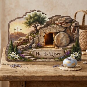 May include: A decorative wooden display featuring a carved stone tomb with a rolled-away boulder, three crosses on a hill at sunrise, and the text He Is Risen. The scene includes green pine trees, white lilies, and purple flowers on a wooden base.
