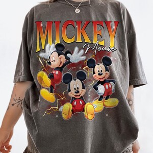 May include: Grey t-shirt featuring Mickey Mouse in three poses with yellow lightning bolts. The text "MICKEY Mouse" is printed in a gradient red and yellow font. The shirt has a vintage style.