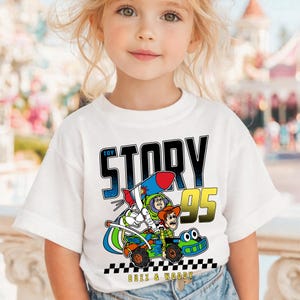 May include: White t-shirt featuring a colorful graphic from the movie Toy Story. The design includes the words "Toy Story 95" and images of Buzz Lightyear, Woody, and a race car. The text "Buzz & Woody" is at the bottom.