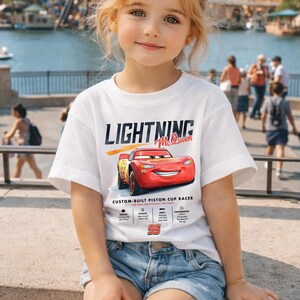 Puede incluir: Una camiseta blanca con el texto "LIGHTNING McQueen" y un coche de carreras rojo de dibujos animados. La camiseta tambi&eacute;n incluye el texto "CUSTOM-BUILT PISTON CUP RACER" y el n&uacute;mero "95".