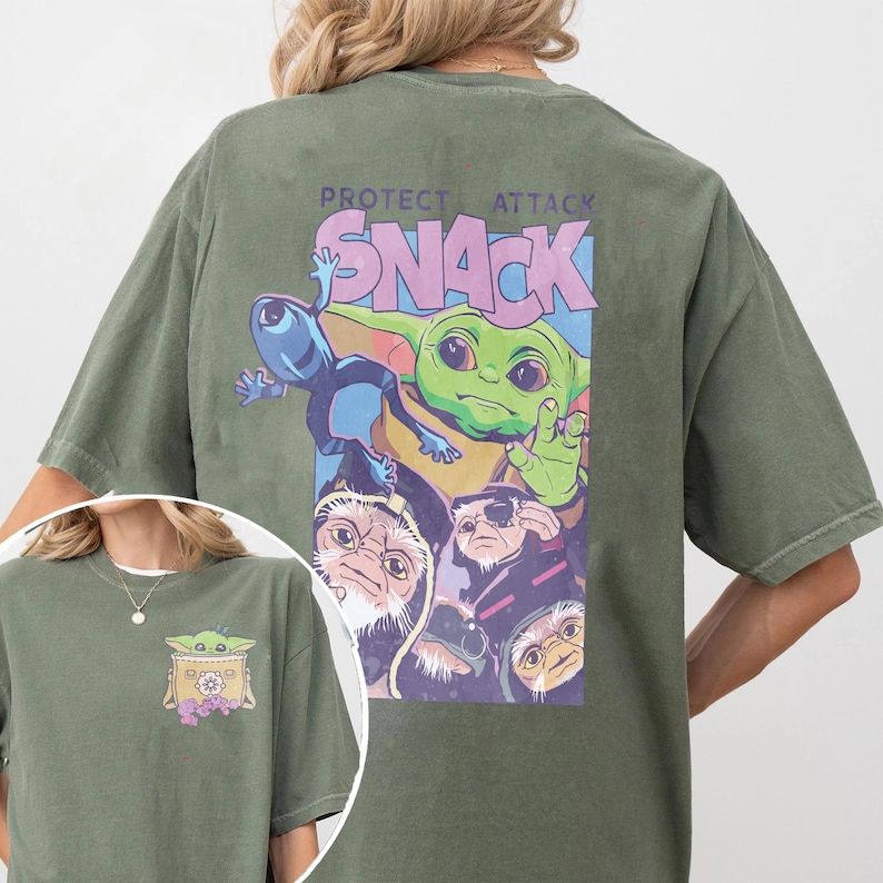 May include: Olive green t-shirt featuring a graphic of a green alien character with the text "PROTECT ATTACK SNACK". The graphic includes other characters in a purple and blue design. A smaller version of the graphic is on the front.