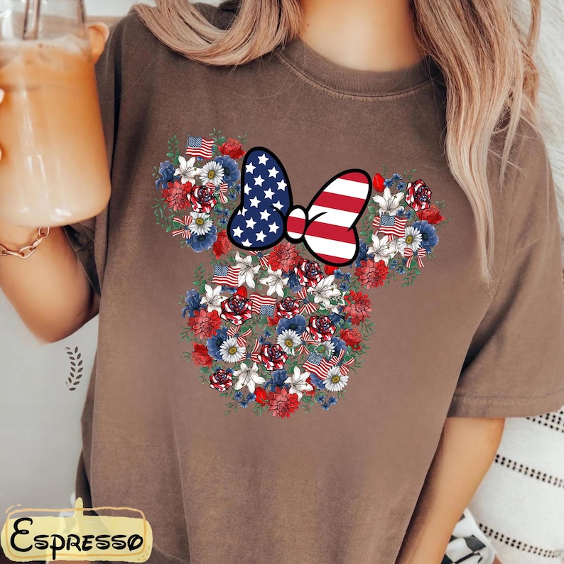 May include: Brown t-shirt featuring a floral design in the shape of a mouse head. The design incorporates red, white, and blue flowers, American flags, and a bow with a stars and stripes pattern. The word "Espresso" is at the bottom.