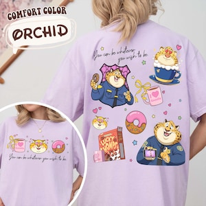 May include: Orchid-colored t-shirt with cartoon leopard illustrations. The shirt features a leopard in a police uniform, a donut, a coffee cup, and the text "You can be whatever you wish to be."