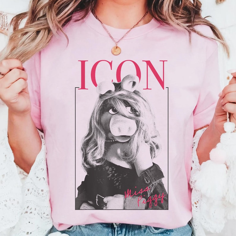 May include: A light pink t-shirt featuring a black and white image of Miss Piggy with the word "ICON" above her and "Miss Piggy" below. The Muppets character is wearing a black jacket and a pearl necklace.