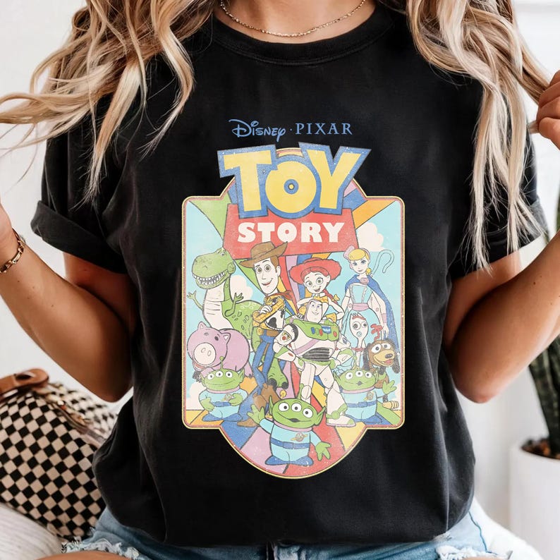 Puede incluir: Camiseta negra con un gr&aacute;fico colorido de personajes de la pel&iacute;cula de Disney Pixar "Toy Story". El dise&ntilde;o incluye el t&iacute;tulo de la pel&iacute;cula y personajes como Woody, Buzz Lightyear y los peque&ntilde;os hombres verdes. La camiseta tiene cuello redondo y mangas cortas.