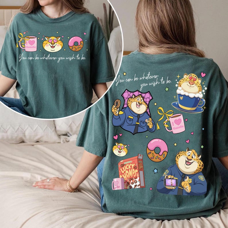 May include: Teal-colored graphic t-shirt featuring a cartoon leopard design with a donut, coffee cup, and the text "You can be whatever you wish to be." The back of the shirt has additional leopard illustrations and text.