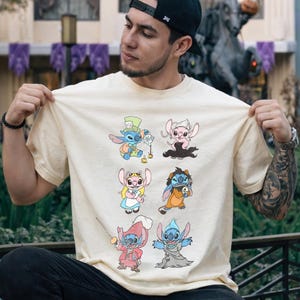 Puede incluir: Una camiseta de manga corta de color crema con un estampado gr&aacute;fico de seis personajes de dibujos animados. El dise&ntilde;o muestra a Stitch y Angel disfrazados de varias figuras, incluyendo el Sombrerero Loco, Alicia y un pirata.