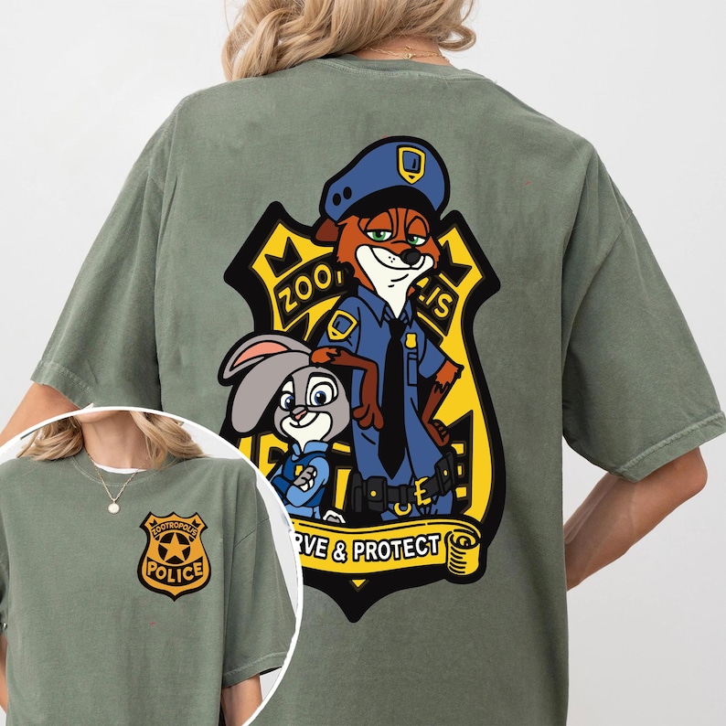 May include: Olive green t-shirt with a cartoon graphic of a fox and a rabbit in police uniforms, with the text "Zootopia Police" and "Serve & Protect". A smaller police badge is on the front of the shirt.