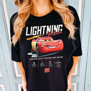 Puede incluir: Camiseta negra con un dise&ntilde;o de Rayo McQueen de la pel&iacute;cula Cars. El gr&aacute;fico incluye el texto "LIGHTNING McQueen" y una imagen del coche de carreras rojo. Tambi&eacute;n se muestran detalles t&eacute;cnicos y el n&uacute;mero 95.