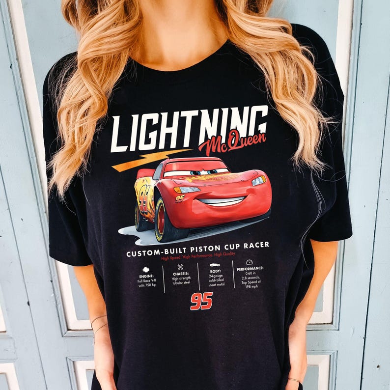 Puede incluir: Camiseta negra con un dise&ntilde;o de Rayo McQueen de la pel&iacute;cula Cars. El gr&aacute;fico incluye el texto "LIGHTNING McQueen" y una imagen del coche de carreras rojo. Tambi&eacute;n se muestran detalles t&eacute;cnicos y el n&uacute;mero 95.