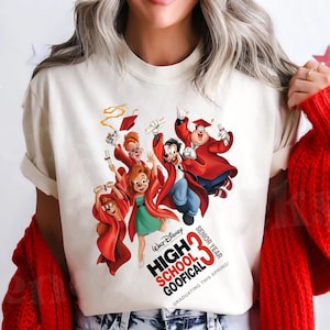 May include: Cream-colored t-shirt featuring a graphic of Disney's High School Goofical characters in graduation attire. The design includes the text "High School Goofical Senior Year 33" and "Graduating this Spring!"