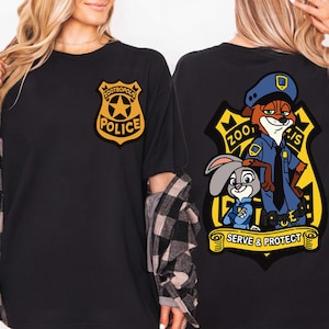 May include: Black t-shirt with a Zootropolis Police badge on the front and a larger graphic on the back. The back graphic features Nick Wilde and Judy Hopps in police uniforms, with the words "Zootropolis" and "Serve & Protect".