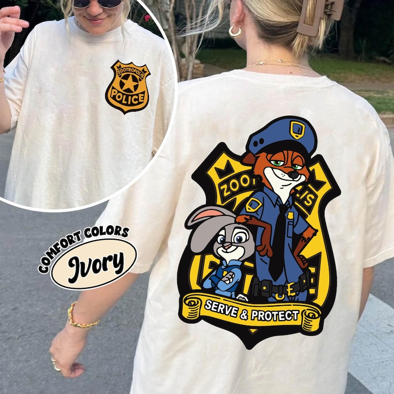 May include: Ivory t-shirt with a cartoon police badge on the front and a larger graphic on the back. The graphic shows a fox and a rabbit in police uniforms, with the text "Zootropolis Police" and "Serve & Protect".