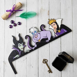 May include: A decorative scene featuring Disney villains Maleficent, Ursula, and the Evil Queen. The scene includes a scroll tied with a purple ribbon, a green feather, purple gems, a vintage key, and a black jewelry box.
